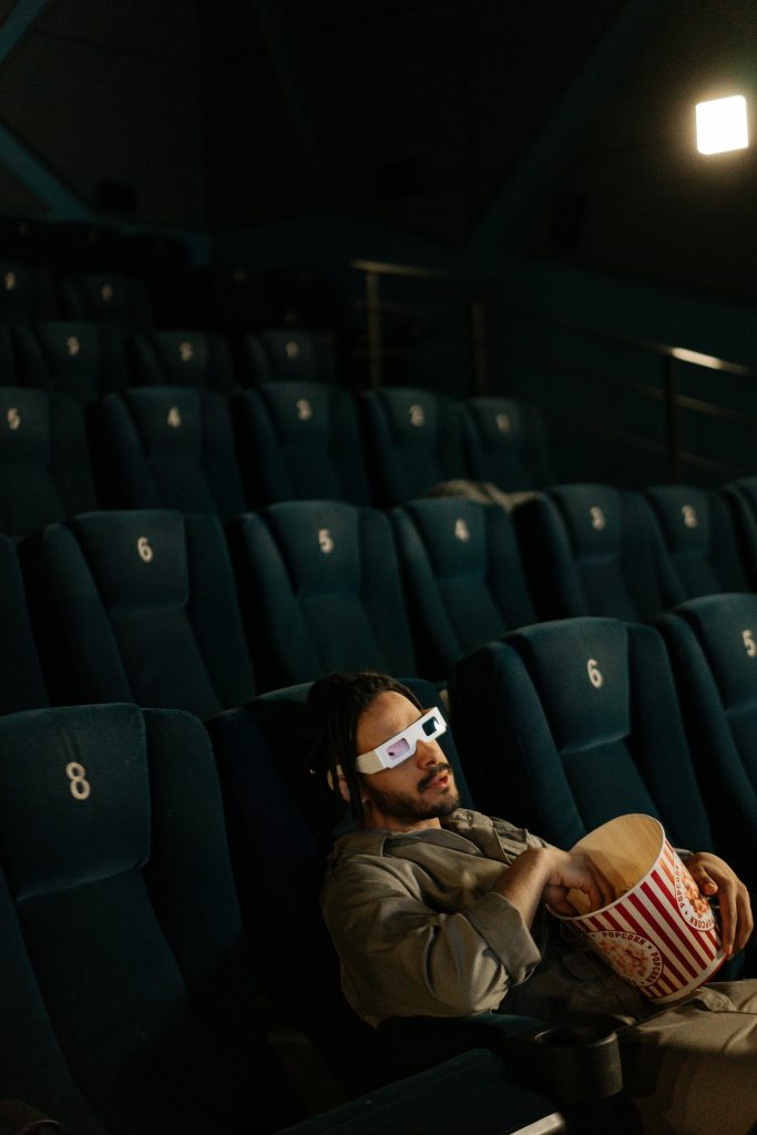 A man enjoys a movie alone in an empty theater, wearing 3D glasses and holding popcorn.